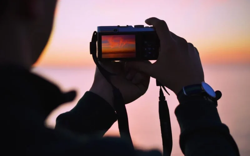 how-to-photograph-a-car-for-sale Person photographing a clean car with a smartphone during golden hour against a plain background
